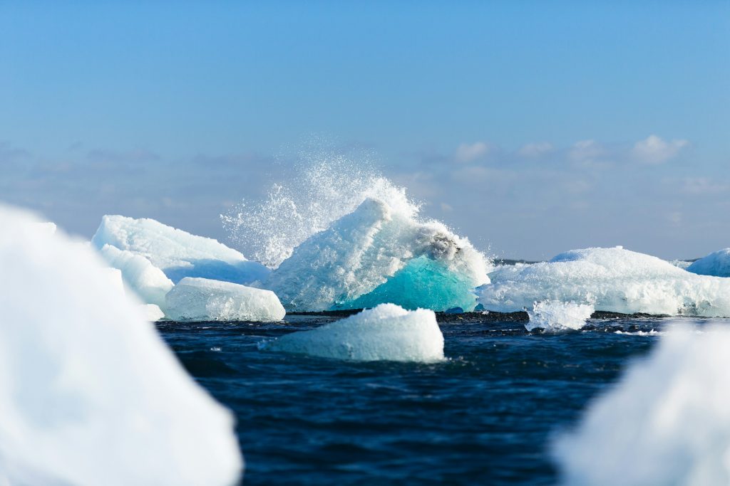 vue sur un glacier d'Islande séparé en plusieurs morceaux flottants sur l'eau, dont une vague se fracassant sur le morceau du milieu.