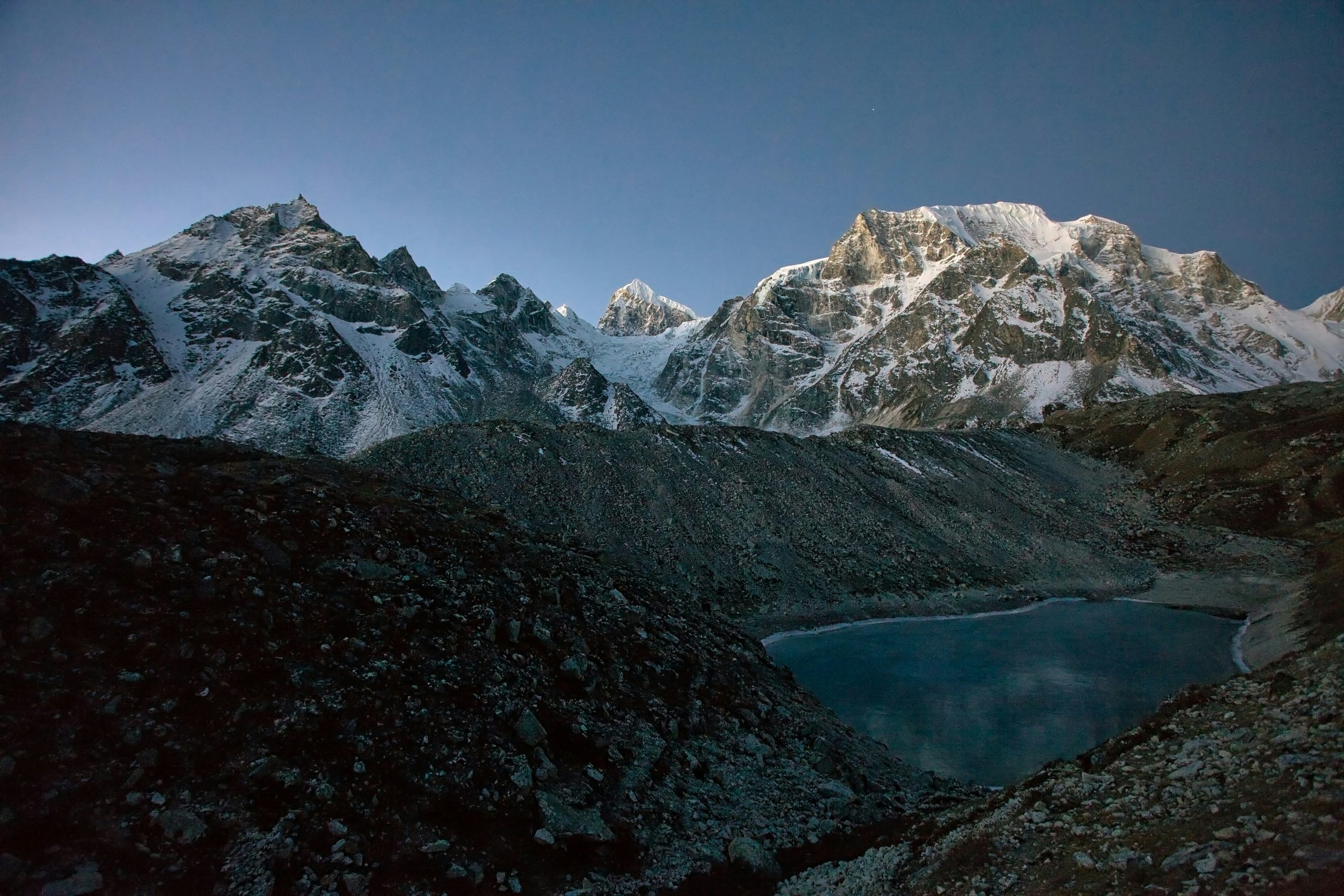 parcours de trek d'un paysage rocheux du Népal, avec des sommets enneigés en arrière plan et un petit point d'eau entouré de collines rocheuses en premier plan